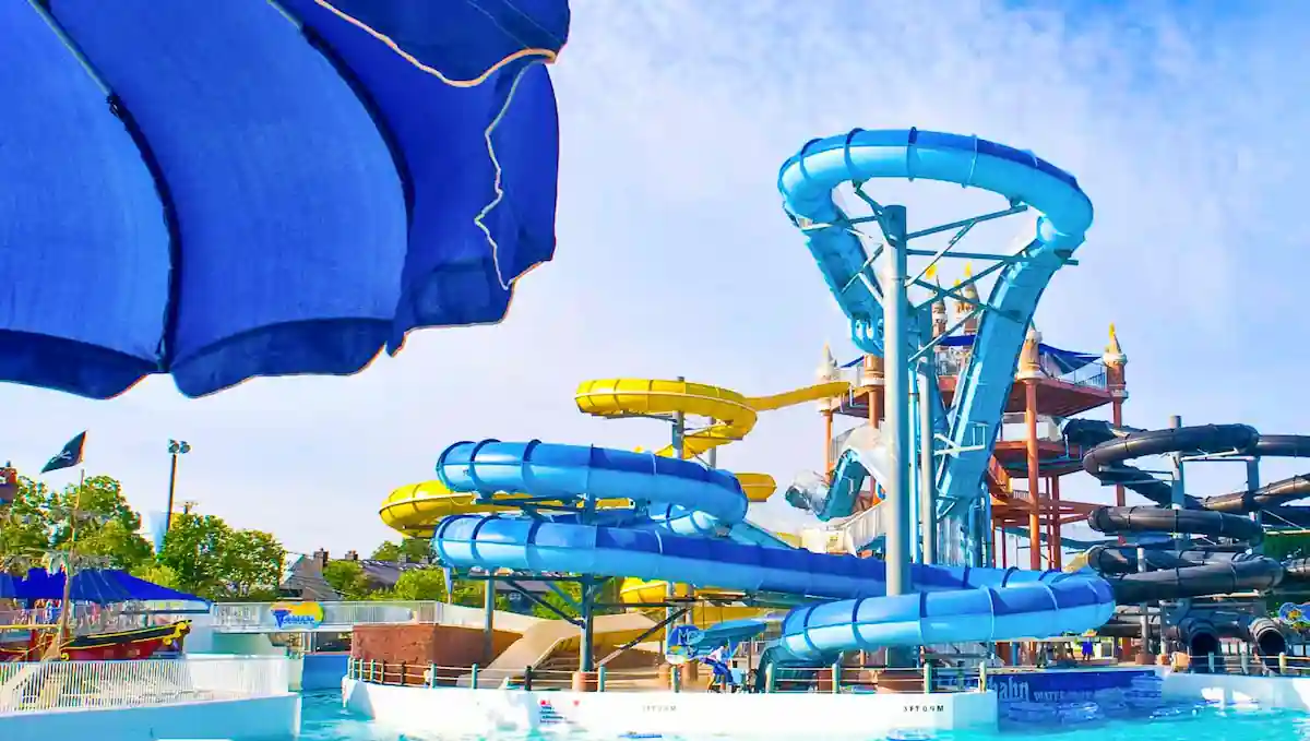 10 Affordable Activities for Kids in Texas 6 A vibrant water park featuring multiple twisting waterslides in blue, yellow, and black, with pools at the bottom. An overhead blue shade structure is partially visible. The clear, sunny sky is in the background, emphasizing a fun, summer atmosphere.