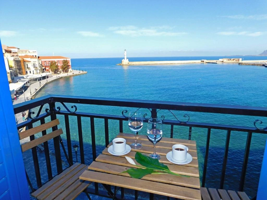 Where to Stay in Portland? 12 Top Rated Places in 2024 9 A balcony overlooking a beautiful waterfront scene. There is a small table with two chairs, coffee cups, and wine glasses on the balcony. A lighthouse and a historic town can be seen in the distance. The water is a vibrant blue, and the sky is clear and sunny.