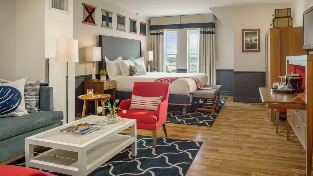 Where to Stay in Portland? 12 Top Rated Places in 2024 12 A spacious hotel room with a nautical theme. The room features a king-size bed with a red throw blanket, a sitting area with a sofa and a coffee table, and a small desk with a minibar. The walls are decorated with nautical-themed artwork, and there is a large window with a view of the water.