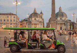 Rome by Golf Cart . A green electric tour cart with five people drives through a lively city square with historic domed buildings, an obelisk, and many pedestrians in the background during the evening.